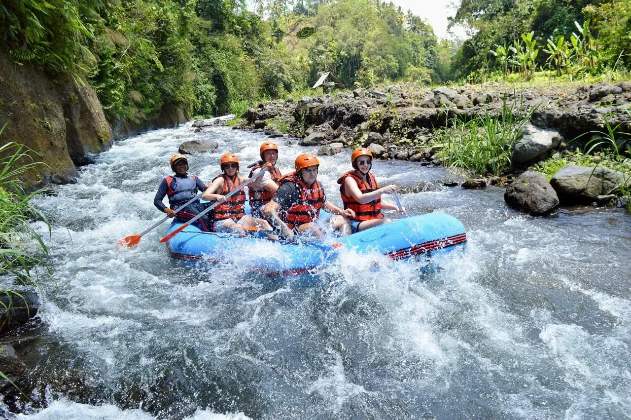 A group of rafters in orange helmets paddling a blue raft through rapids on the Telaga Waja River